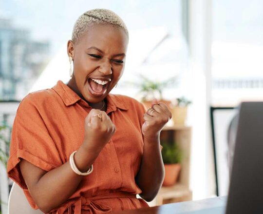 Happy woman at laptop making yes gesture with both hands