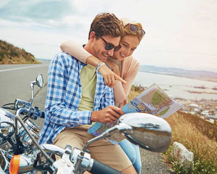 couple sitting on motorcycle viewing map